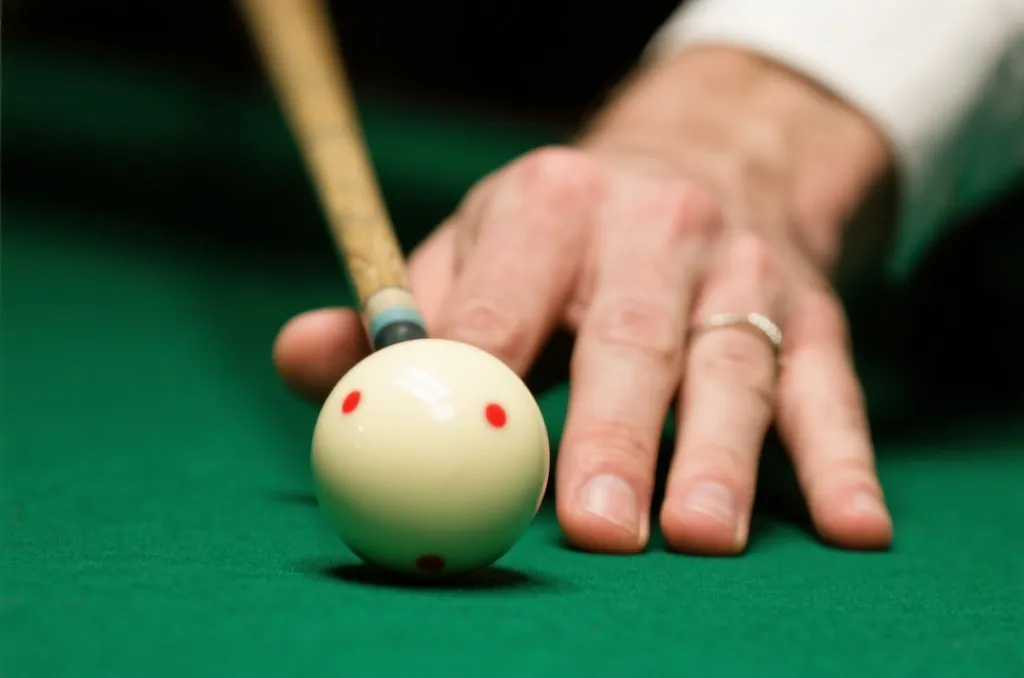 Close-up of a snooker player's hands holding a cue stick, aiming at a white cue ball on a green cloth table